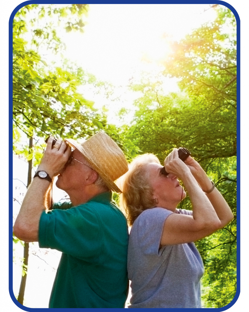 a senior man and woman back to back looking through binoculars - birdwatching