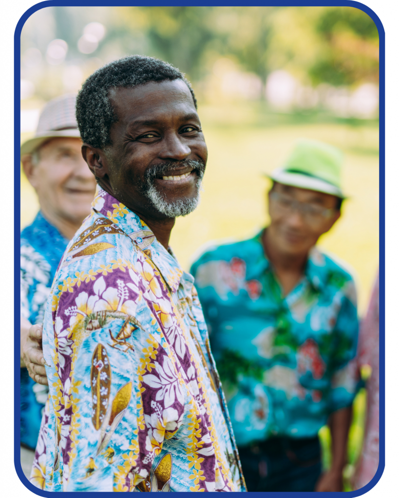 an older african american adult smiles at the camera in a hawaiian styles shirt surrounded by other older adult sin hawaiina shirts.