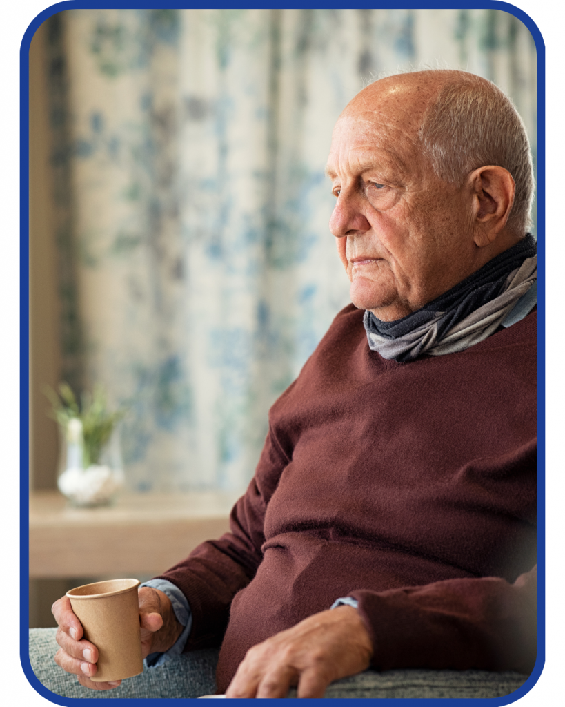 older male adult sits in a chair with a paper cup and looks pensive in a maroon sweater