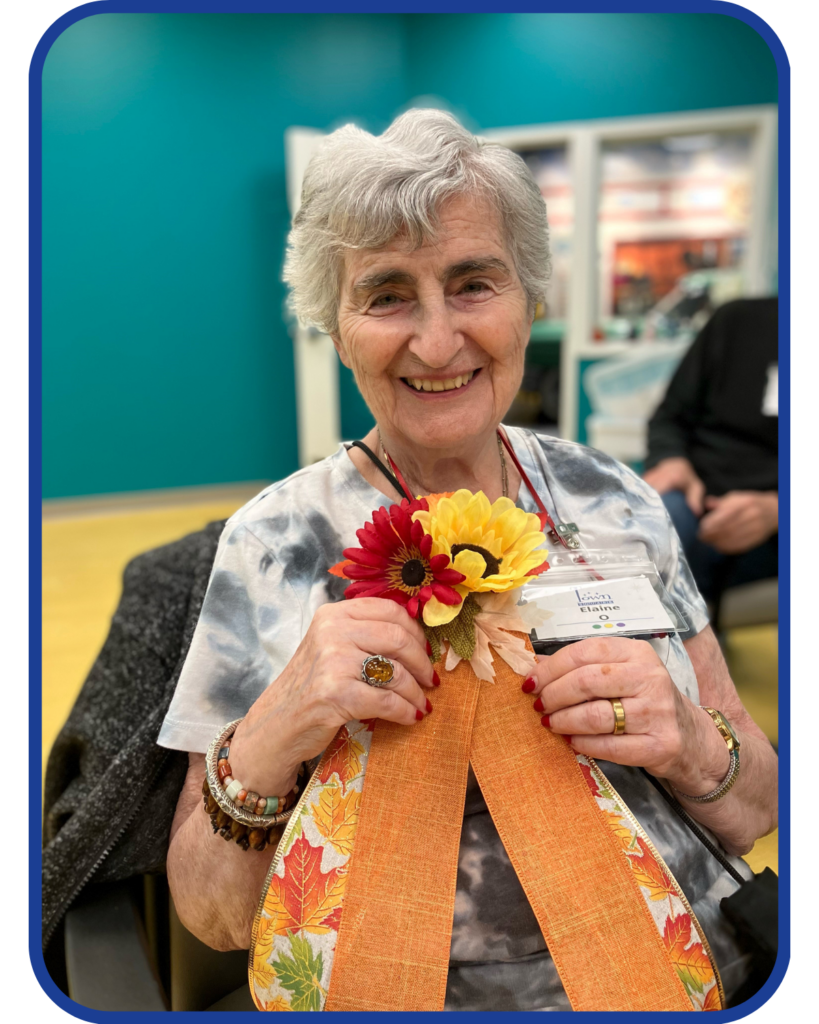 an older female adult holds a fall craft she created at the adult day program she attends