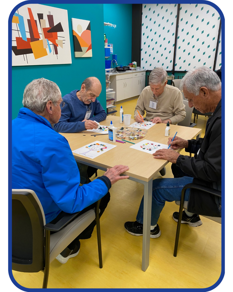 a group of male older adults sit at  table together doing a craft at Adult Day Care