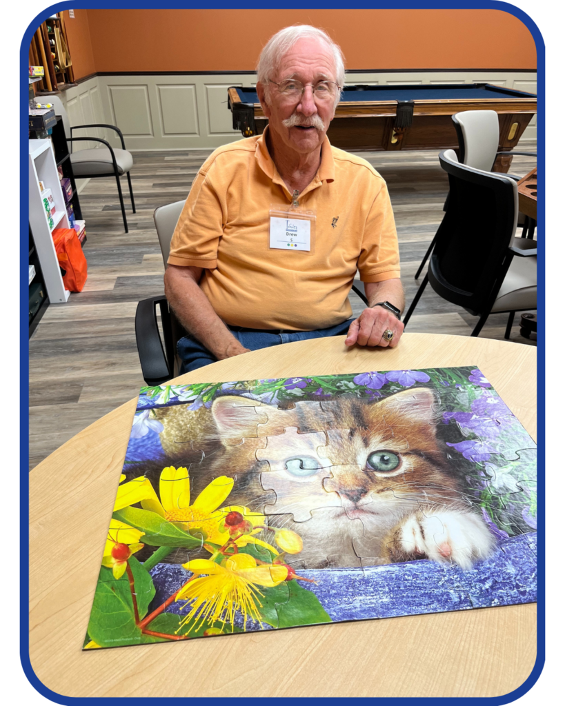 Older Male Adult sitting at a talble in front of the puzzle he just completed.