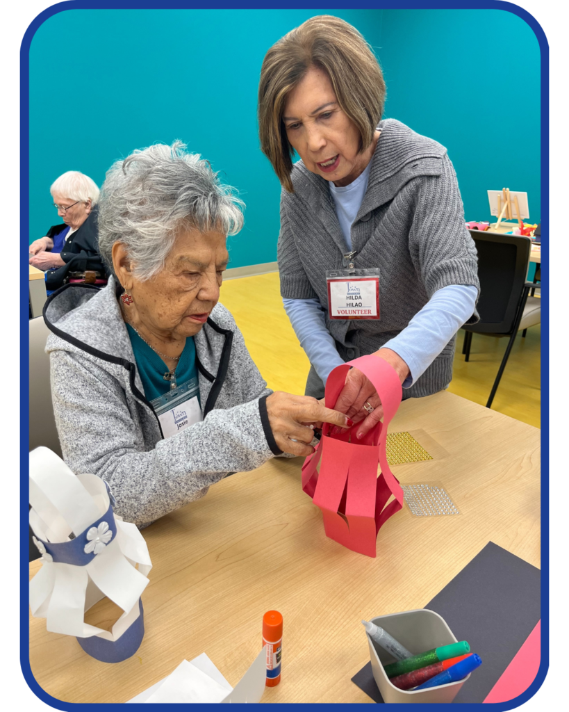 Two female older adults work together on a paper lantern craft at an adult enrichment center