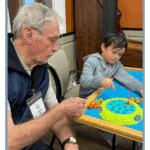 Older adults and young children play a fishing game together at Town Square NW Austin, highlighting intergenerational activities that reduce restlessness and provide purposeful engagement for dementia care.